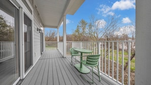 A covered porch with a table and chairs, a white railing, and a view of trees and grass.