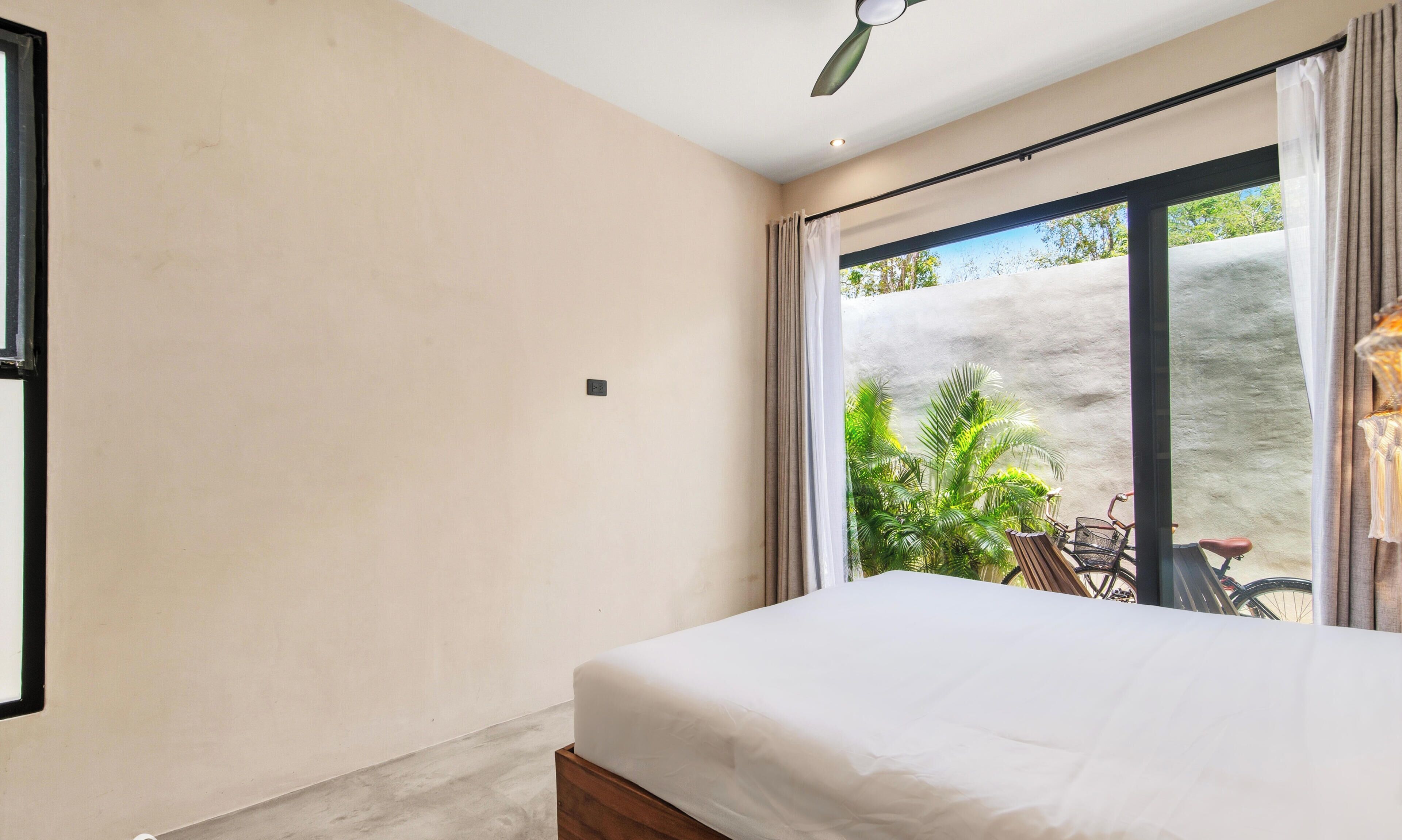 A bedroom with a large bed, a sliding glass door leading to an outdoor area with plants and a bicycle.