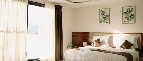 Une chambre d’hôtel avec un grand lit, un ventilateur de plafond et deux reproductions botaniques encadrées accrochées au mur.