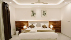 A modern hotel room with a large bed, two bedside tables with lamps, a ceiling fan, and two framed botanical prints on the wall. - The Rainbow Villa (Udaipur)