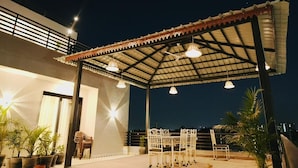 An outdoor patio area with a covered seating area, potted plants, and a railing. - The Rainbow Villa (Udaipur)