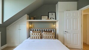 Un dormitorio con una cama, almohadas estampadas, una puerta blanca y una repisa con cuadros enmarcados.