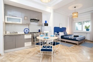 Un espacio habitable compacto con kitchenette, una zona de comedor con una mesa redonda y sillas, una cama con cabecera y un ventanal con vistas.