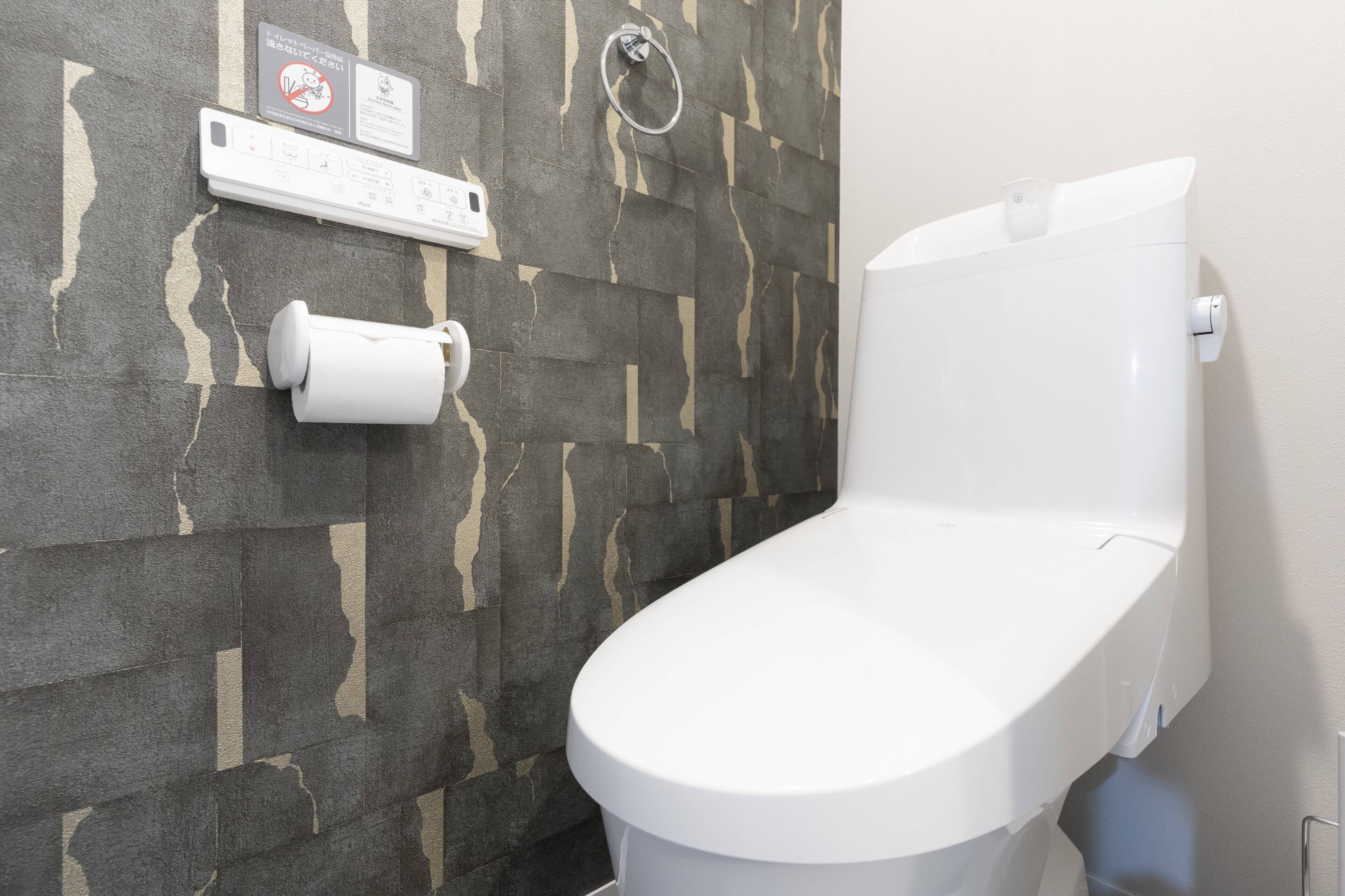 A toilet with a white seat and lid, a toilet paper holder, and a hand sanitizer dispenser on the wall.