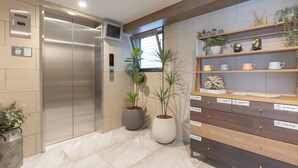 A modern elevator, potted plants, and a storage unit with labeled compartments. - b&Hanazono2 (Bainan, Nishinari Ward,)