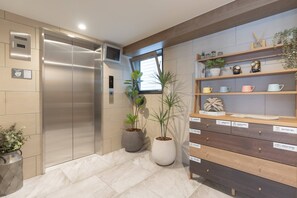 A modern elevator, potted plants, and a storage unit with labeled compartments. - b&Hanazono2 (Bainan, Nishinari Ward,)
