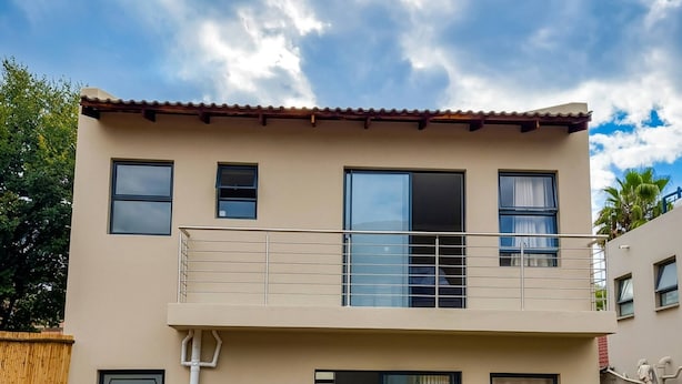Ein zweistöckiges Gebäude mit Balkon, Schwimmbad und Garten.