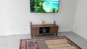 Ein modernes Wohnzimmer mit Flachbildfernseher, Couchtisch aus Holz, gemustertem Teppich und einem schlichten Schrank.