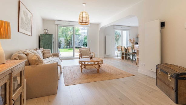 A spacious living room with a sofa, a round table, and a wicker chair. There is a large window providing a view of the outdoors. - Magnificent Apartment - 2br- 6P - Garden - Deauville (Deauville)