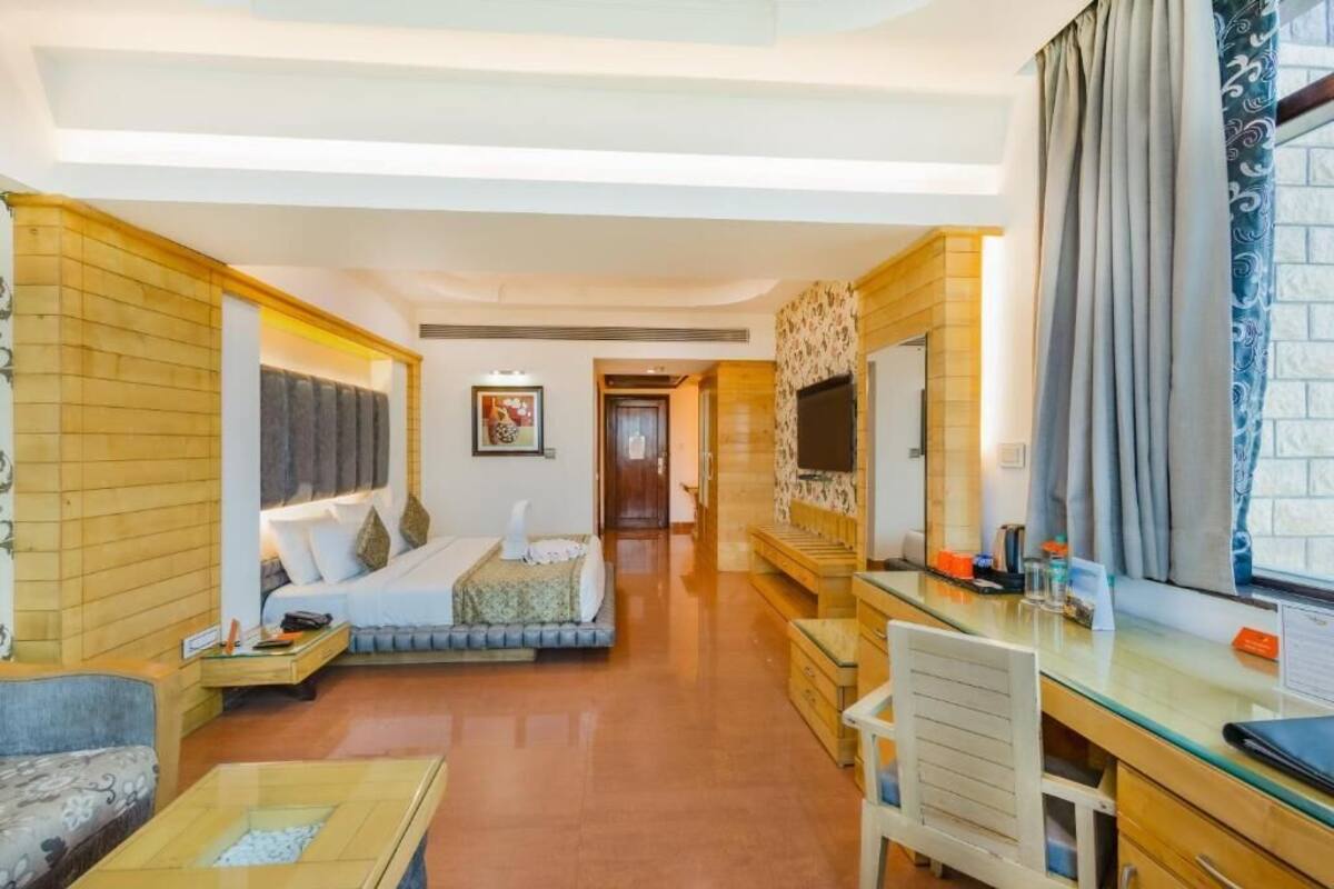 Une chambre d’hôtel avec un lit, un bureau, une chaise et une grande fenêtre avec des rideaux.