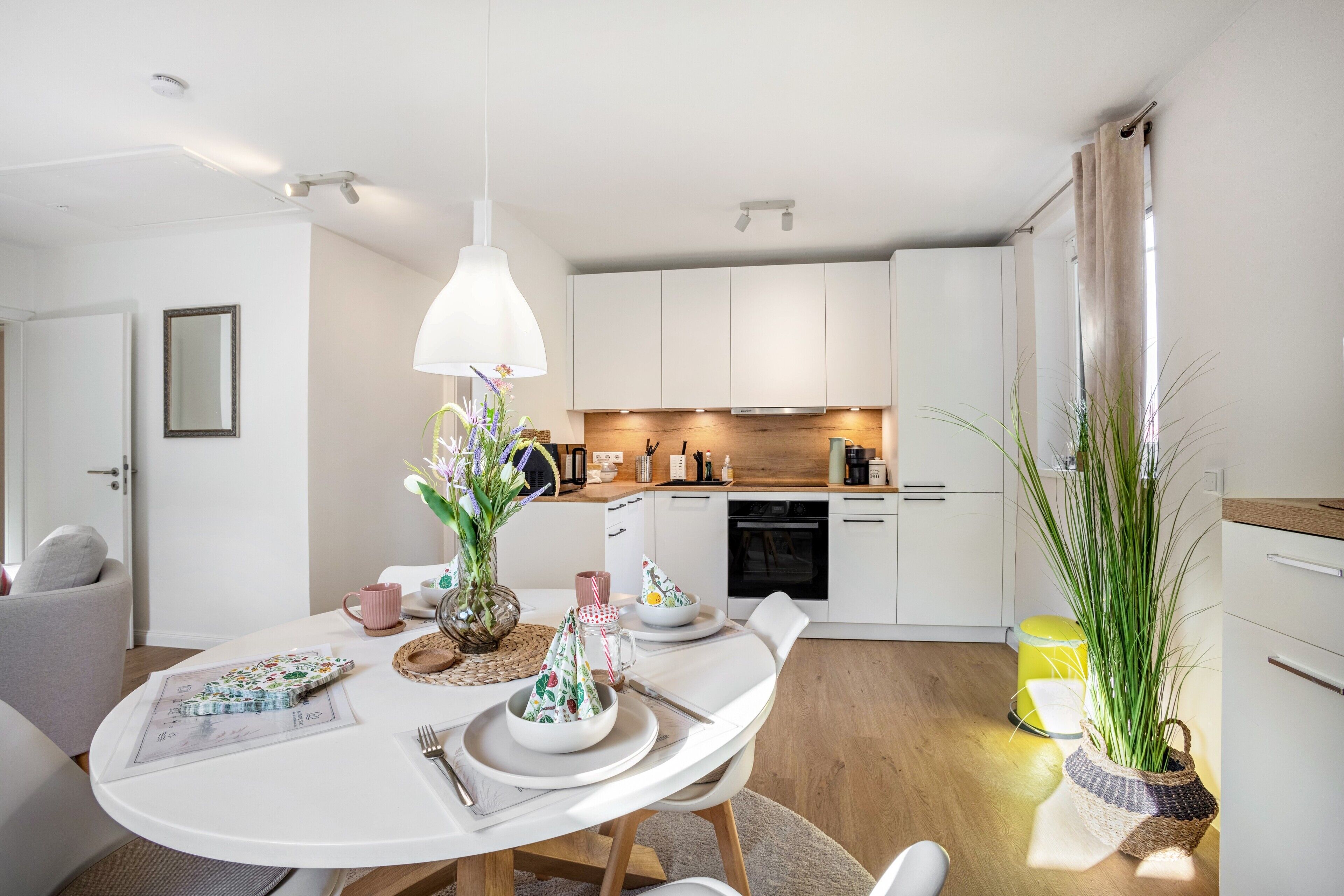 A modern kitchen with white cabinets, a dining table with chairs, and a hanging pendant light.