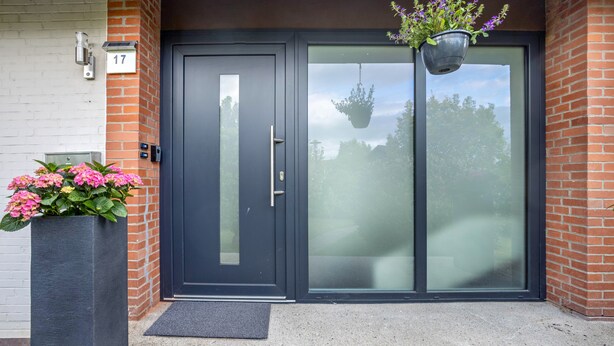 A modern entrance with a dark-colored door, a potted plant with pink flowers, and a hanging planter with purple flowers. - Nordic Stay Bäk: Private Terrace & Garden near Lake Ratzeburg, Lübeck, Mölln (Bäk)