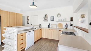 A modern kitchen with wooden cabinets, a dishwasher, a stove, and a hanging light fixture. - 
Country on the Coast (Numbaa)