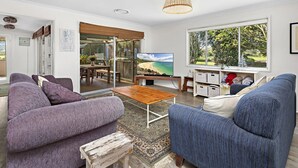 A living room with a television, sofas, a coffee table, and a view of a beach through large windows. - 
Country on the Coast (Numbaa)