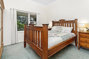 Ein Bett mit Holzkopf, ein Nachttisch, eine Lampe und ein Fenster mit Vorhängen.