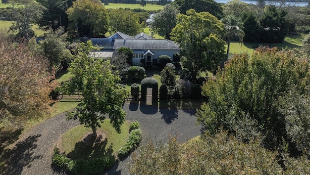 A large house surrounded by a well-maintained garden with a pond, trees, and a view of a lake and hills in the distance. - 
Country on the Coast (Numbaa)