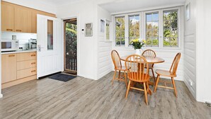 A kitchen with wooden cabinets, a microwave, and a coffee maker. There is a dining area with a round table and four wooden chairs. - 
Country on the Coast (Numbaa)