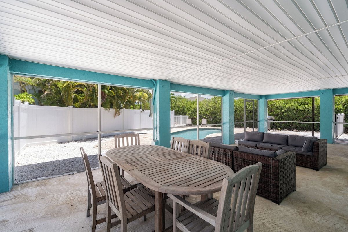 Un espacio exterior cubierto con piscina, una mesa de comedor con sillas y una zona de estar con sofás.
