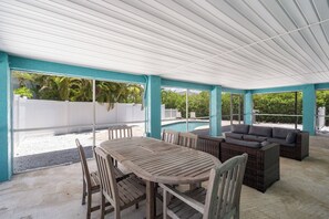 Ein überdachter Außenbereich mit Pool, Esstisch mit Stühlen und einer Sitzecke mit Sofas.