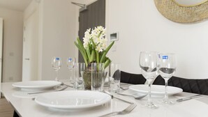 Ein Esstisch ist gedeckt mit Tellern, Besteck und Gläsern, eine Vase mit Blumen und ein dekorativer Spiegel an der Wand.