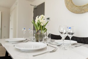 A dining table set with plates, cutlery, and glasses, a vase with flowers, and a decorative mirror on the wall. - Modern 2-Bed Flat 70 at Sapphire Court, Birmingham (West Midlands)