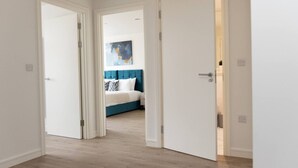 Ein Flur, der zu einem Schlafzimmer mit Bett, Gemälde und einer weißen Tür führt.