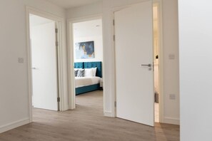 A hallway leading to a bedroom with a bed, a painting, and a white door. - Modern 2-Bed Flat 70 at Sapphire Court, Birmingham (West Midlands)