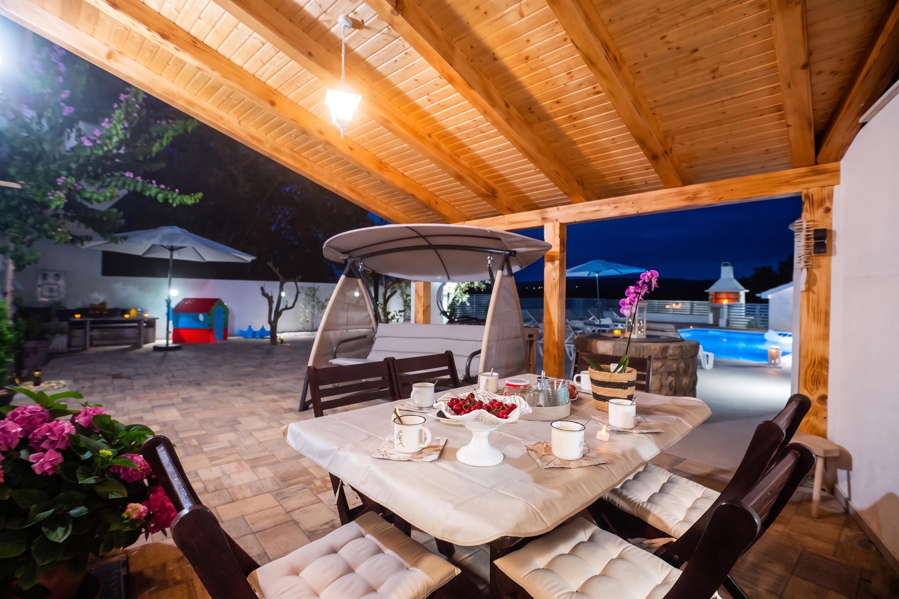 An outdoor dining area with a table set for two, surrounded by wooden chairs and a canopy.