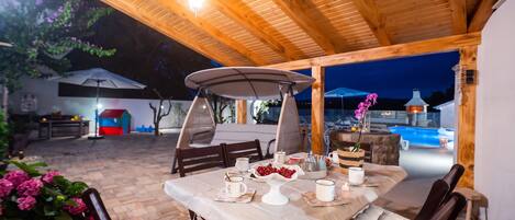 An outdoor dining area with a table set for two, surrounded by wooden chairs and a canopy.
