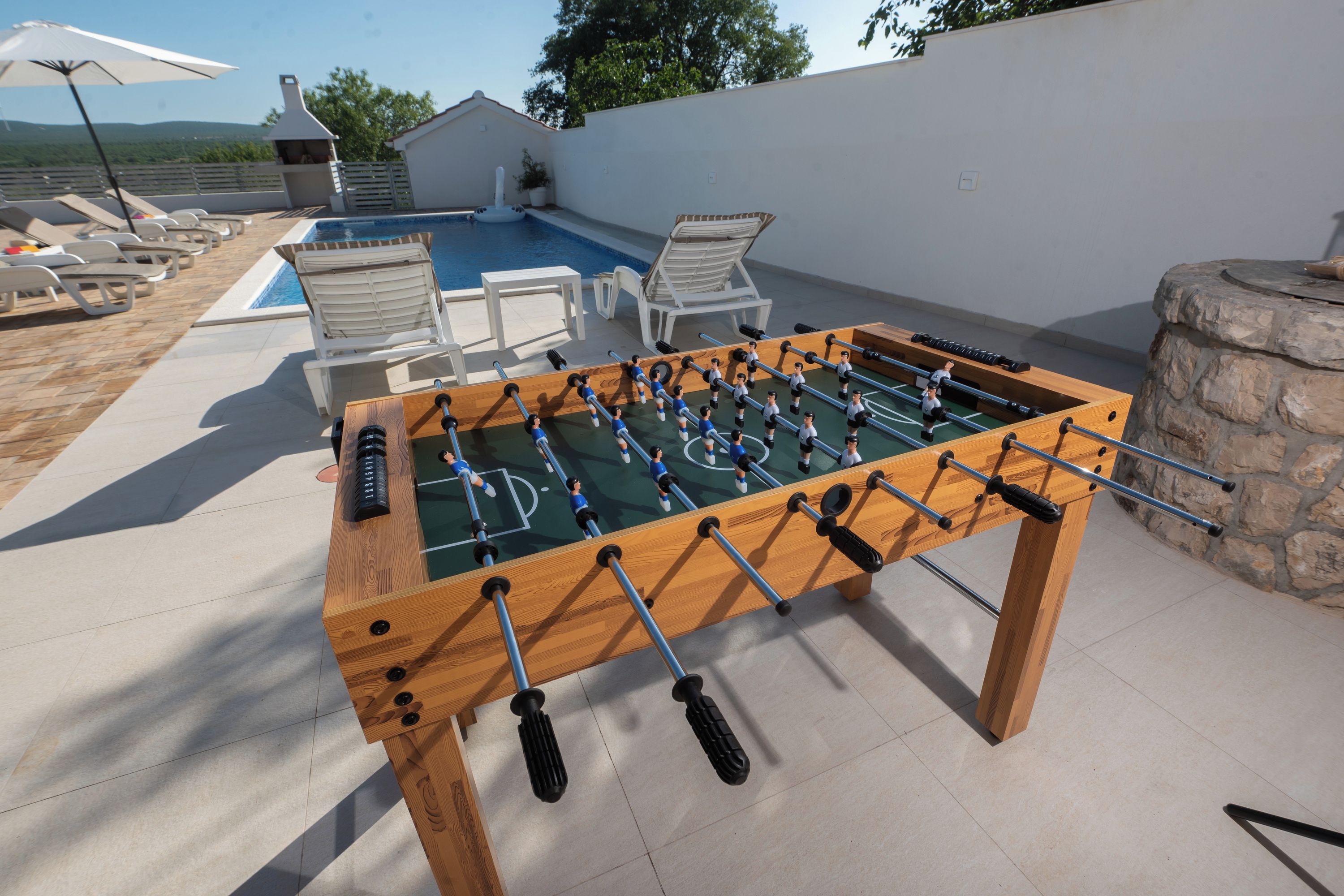 A foosball table with a pool table nearby, outdoor seating, and a stone wall.