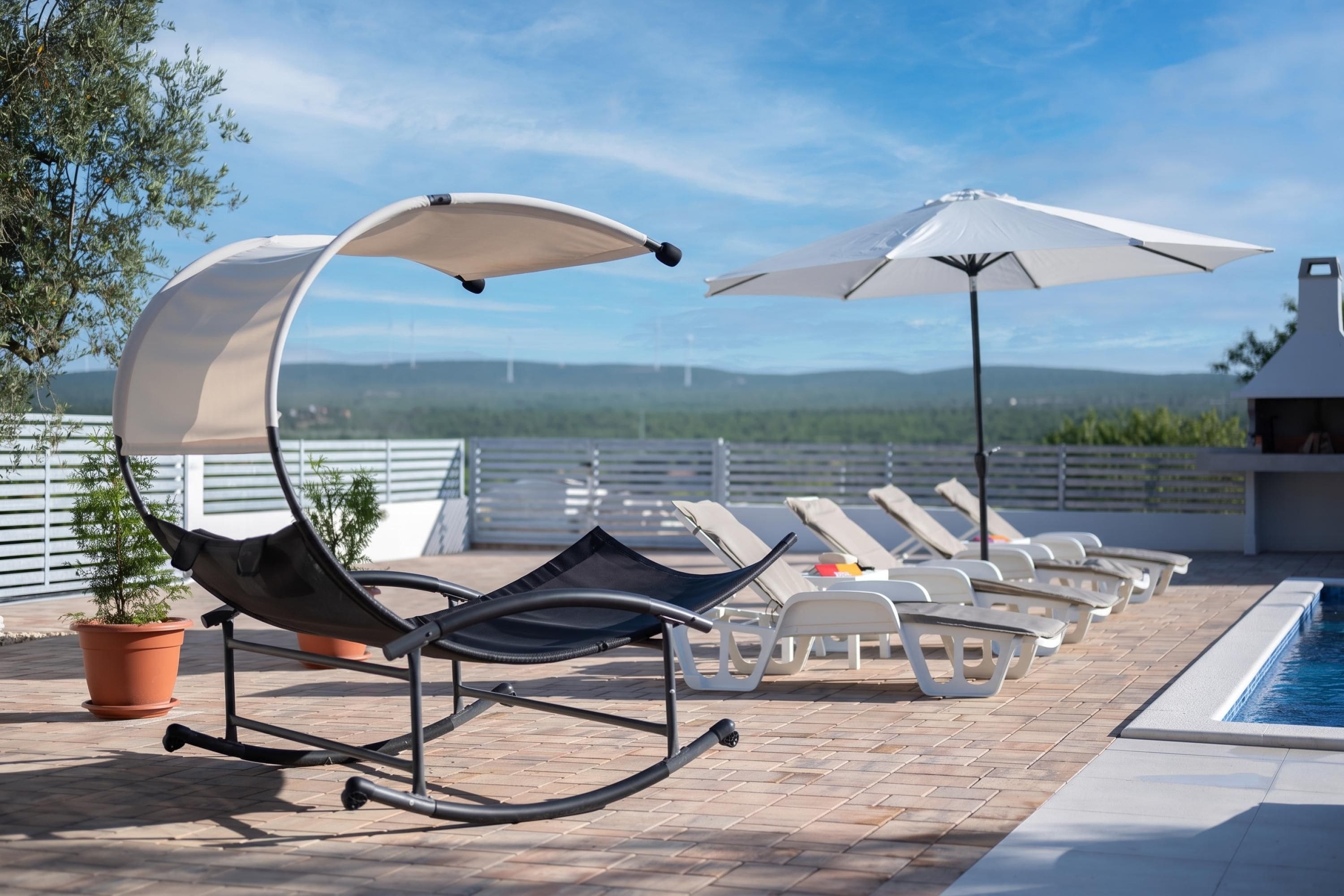 Ein Poolbereich auf dem Dach mit Liegestühlen, Sonnenschirmen und Blick auf die Landschaft.
