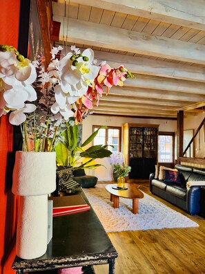A room with a wooden floor, a black table with a white vase, a sofa, and a staircase. - La Maison Rouge Riquewihr (Riquewihr)
