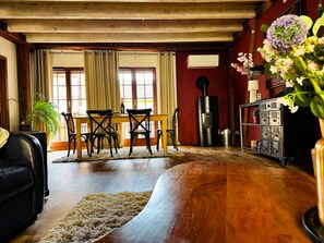 A room with a wooden floor, a dining table with chairs, a sofa, a fireplace, and a cabinet with decorative items. - La Maison Rouge Riquewihr (Riquewihr)
