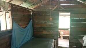 A wooden cabin with a bed, a hammock, and a window.
