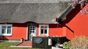 Una casa tradicional con techo de paja, fachada roja, una puerta verde y un pequeño porche.
