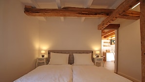 Una cama doble con dos mesitas de noche, una viga de techo de madera y un pasillo que conduce a otra habitación.