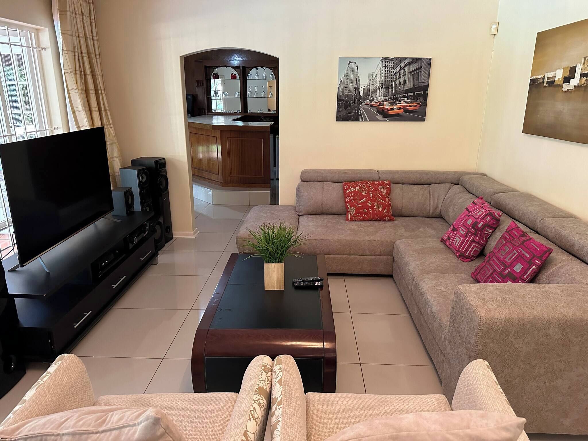 A living room with a TV, sofa, coffee table, and a kitchen in the background.