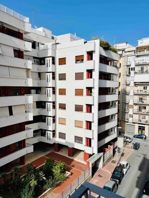 A multi-story residential building with balconies, a parking area, and a clear sky. - Apartment by the Sea (Bari)