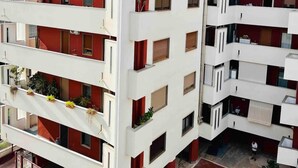 Un immeuble résidentiel à plusieurs étages, doté de balcons, d’un toit plat et d’une entrée sécurisée par un portail.