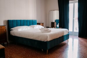 A neatly made bed with a teal headboard and white bedding in a room with a polished floor and a large window with curtains. - Apartment by the Sea (Bari)