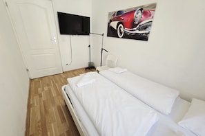 Ein Zimmer mit einem Bett, einem an der Wand befestigten Fernseher und einem Bild von einem Auto.