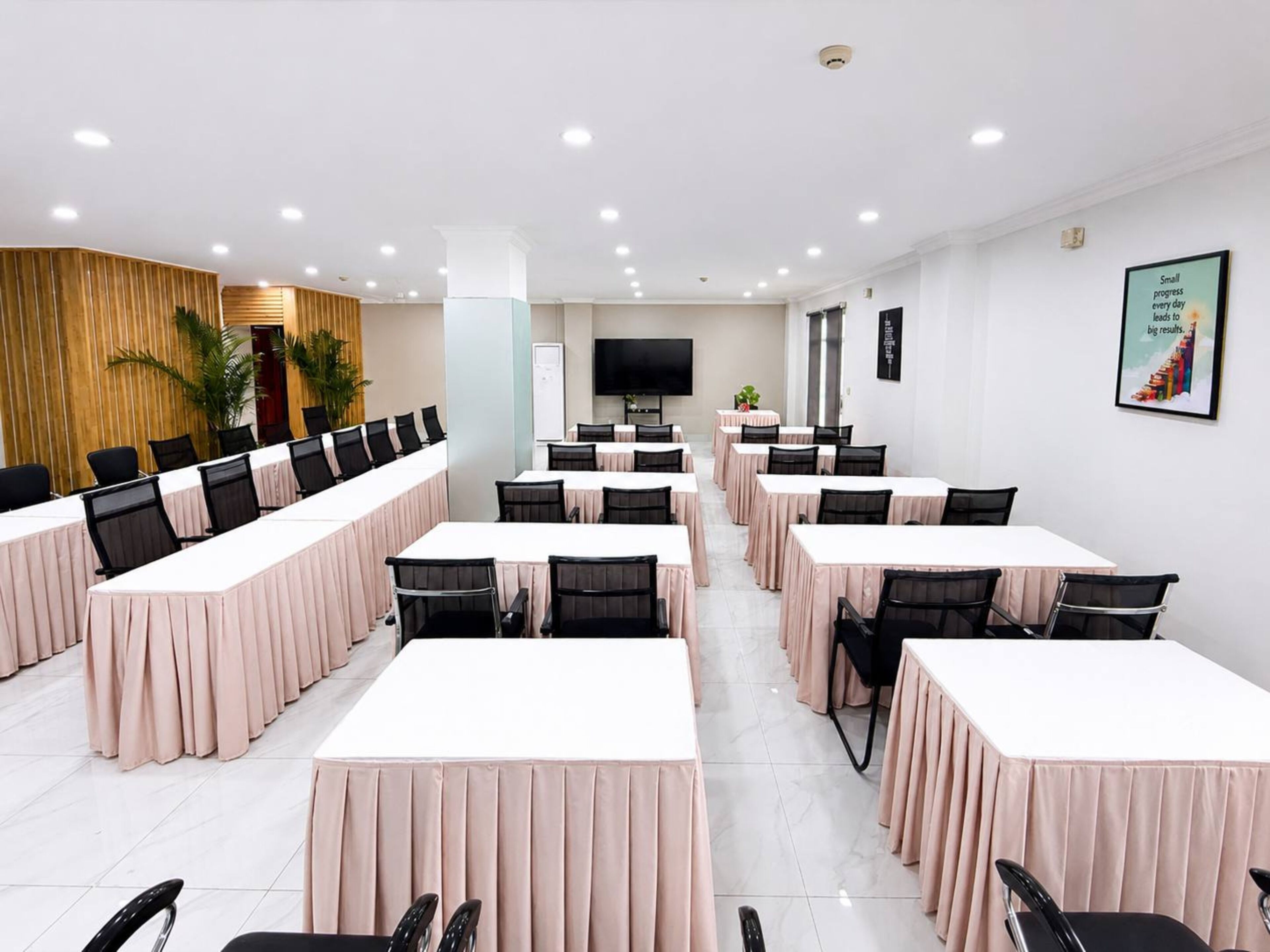 Une salle de conférence équipée de plusieurs tables et chaises, d’un téléviseur et d’une plante.