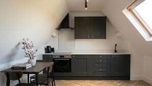 Cocina compacta con armarios oscuros, encimera blanca, horno empotrado y un pequeño comedor con mesa y sillas de madera.