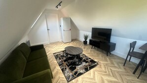 Un salón estilo loft con suelo en espiga, un sofá verde, una mesa de centro redonda, un televisor y una zona de comedor con sillas.