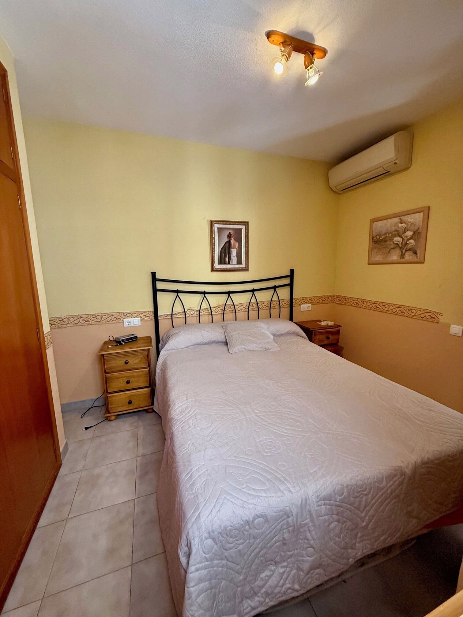 Um quarto com uma cama, mesa de cabeceira, cômoda, ar condicionado e luminária no teto.
