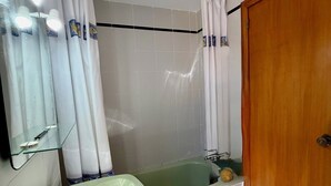 Ein Badezimmer mit einem grünen Waschbecken, einer Badewanne, einer Holztür und weiß gefliesten Wänden.
