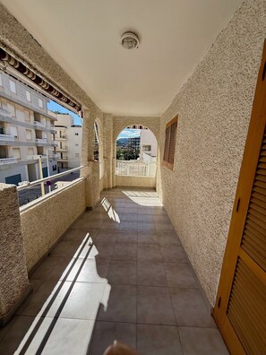 Un pasillo con suelo de baldosas, una lámpara en el techo y vistas de edificios a través de un arco.