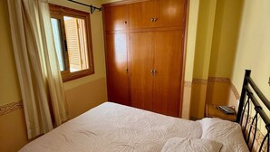 Ein Schlafzimmer mit Bett, Kleiderschrank, einem Fenster mit Vorhängen und einer Deckenleuchte.