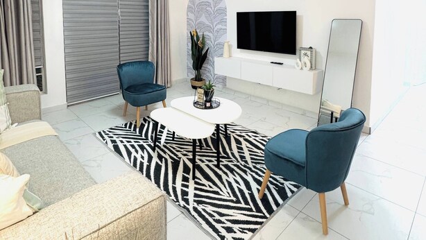 Uma sala de estar moderna com um sofá, duas poltronas, uma mesa de centro, uma televisão e um espelho grande.