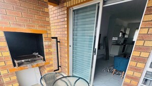 Um pátio com parede de tijolos, porta de vidro deslizante que dá para uma cozinha e duas cadeiras de vime.